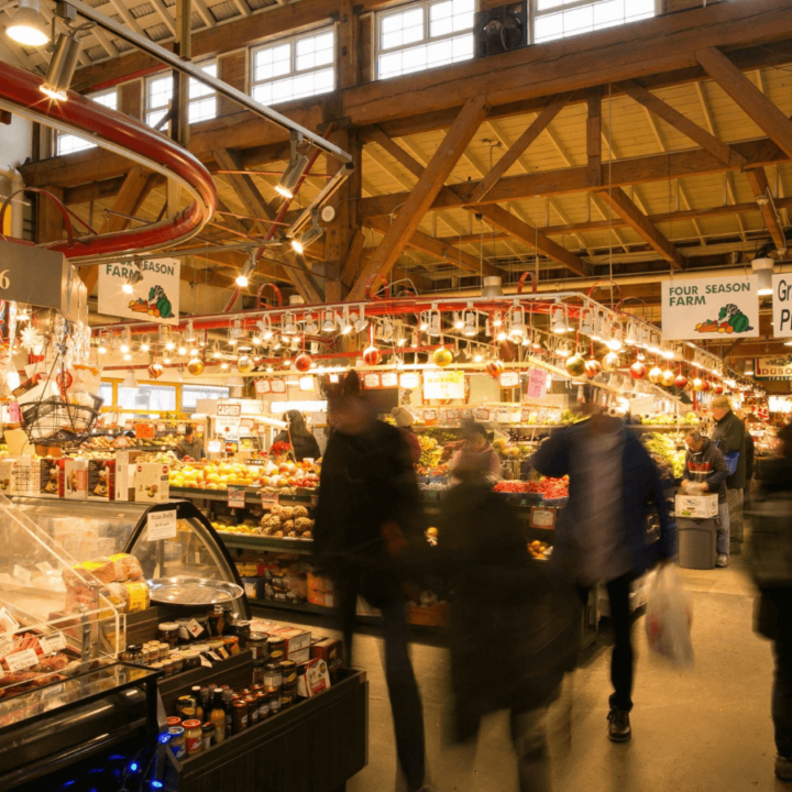 An image of the produce stands inside the Public Market, on Granville Island, with customers shopping and walking around.