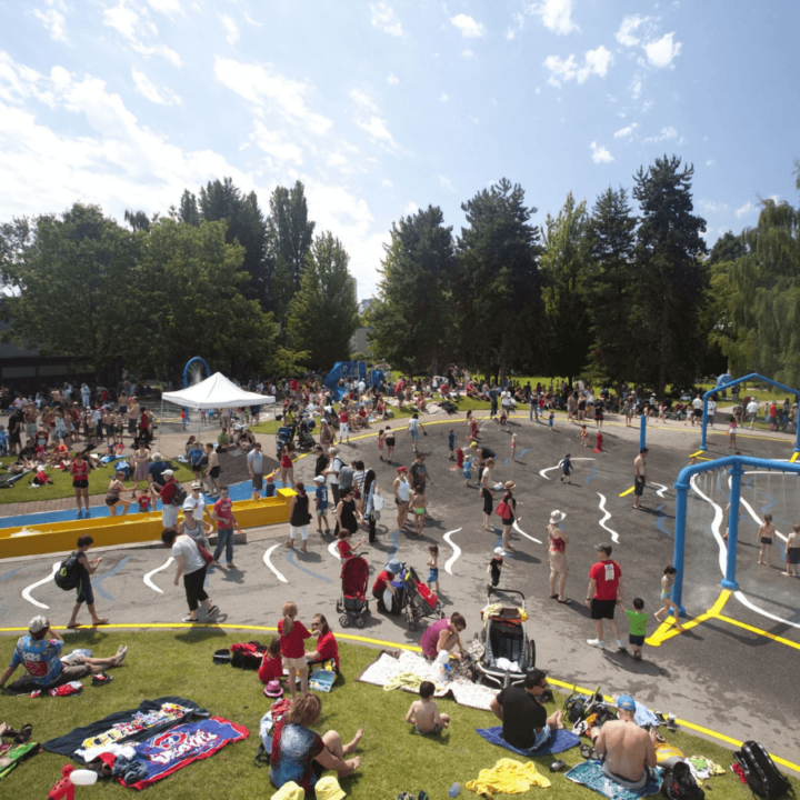 A picture of the waterpark at Sutcliffe Park on Granville Island. There are lots of kids and families running and playing in the sprinklers.