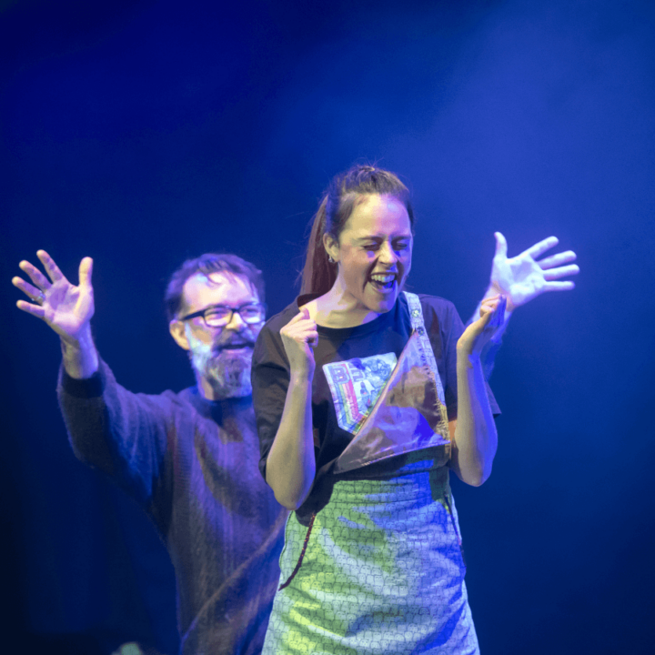 A man and woman on stage with their arms outstretched.