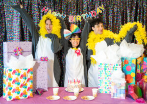 Three people dressed up as penguins at a birthday party.