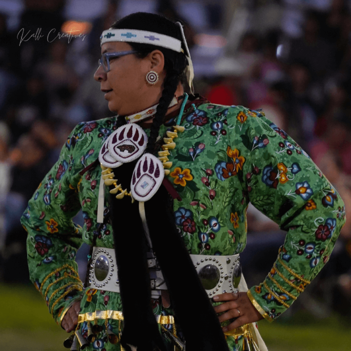 An Indigenous female dancer in a traditional regalia standing in front of a crowd.