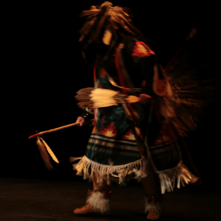 An Indigenous dancer in traditional regalia on stage.