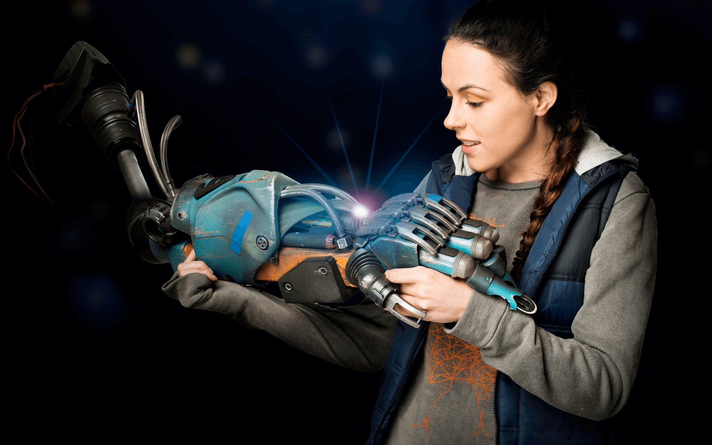 A female actor as a girl is looking down at a blue robot arm she is holding.