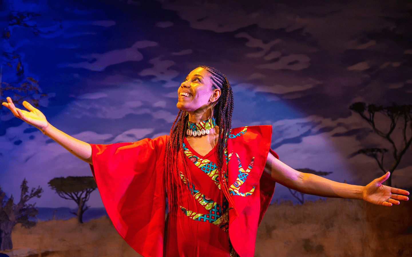 A woman in a red traditional African clothing with her arms outstretched and looking up.