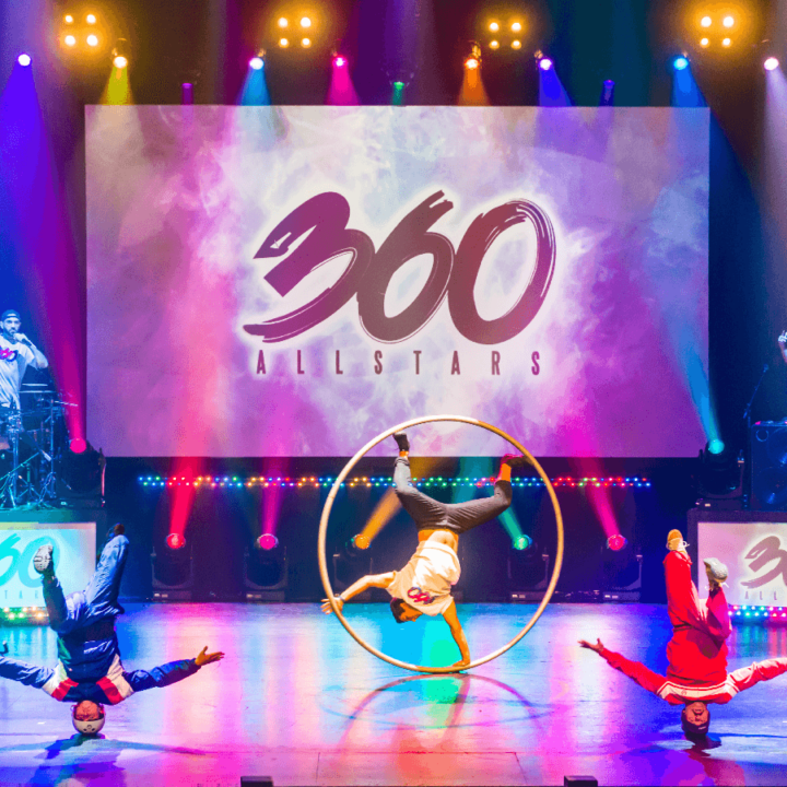 A group of people performing on a stage with a hoop in the background. The words 360 AllStars is projected behind them on a screen.