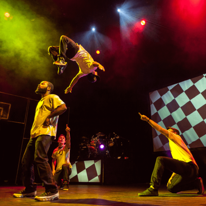 A man doing a back flip on stage. A another man is crouching beside him pointing.