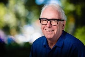 A photograph of a man (Norman Armour) in a blue shirt and black-rimmed eyeglasses, smiling.