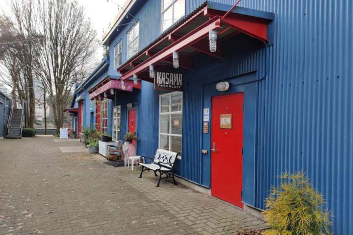 A photograph showing a blue building with a red door that leads to Kasama Chocolate. In the background you can see the entrance for Bon Macaron Patisserie Ltd.