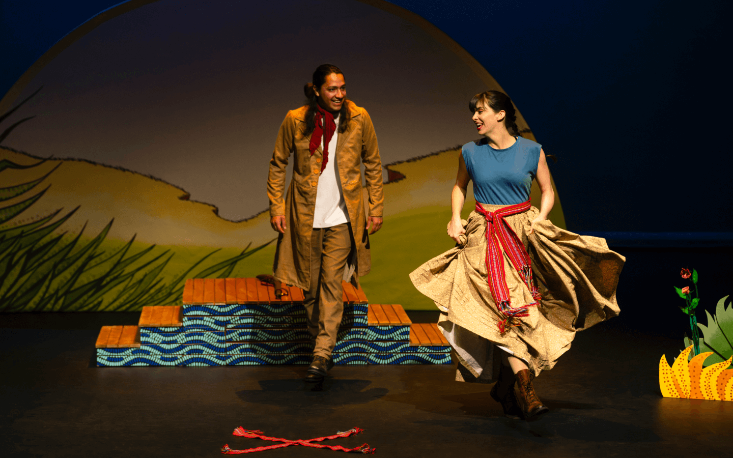 Marie, a Métis woman and Louis Callihoo, the famous Suntraveller are dancing the Red River Jig. Marie’s skirt is flowing. Two red sashes make an X on the floor in front of them.