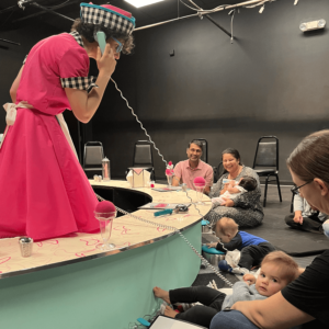 Dottie is talking on a mint green landline telephone with a very long cable. Parents and kids are watching and laughing. There are ice cream sundaes made of felt on the counter.